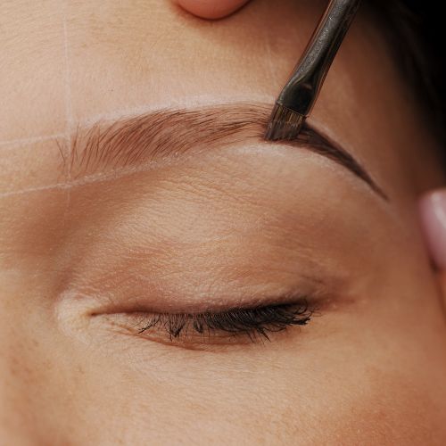 Kosmetikerin formt oder färbt Augenbraue mit feinem Pinsel für präzises Brauenstyling