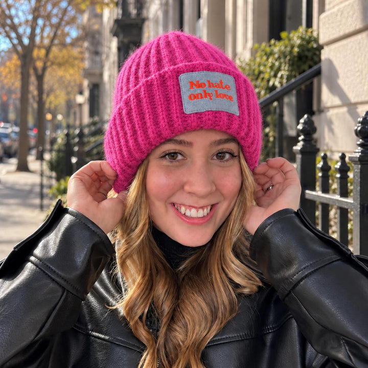 Blonde Frau trägt CASHIMAR Mütze Ancona in Pink mit „No Hate Only Love“-Patch im Outdoor-Look in schwarzer Lederjacke