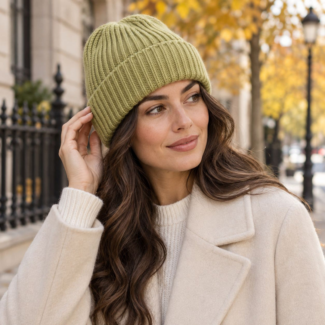 Model mit langen dunklen Haaren trägt die Cashimar Cashmere Mütze Bari in Absinthe (Lime) mit cremefarbenem Mantel im herbstlichen Outdoor-Setting.