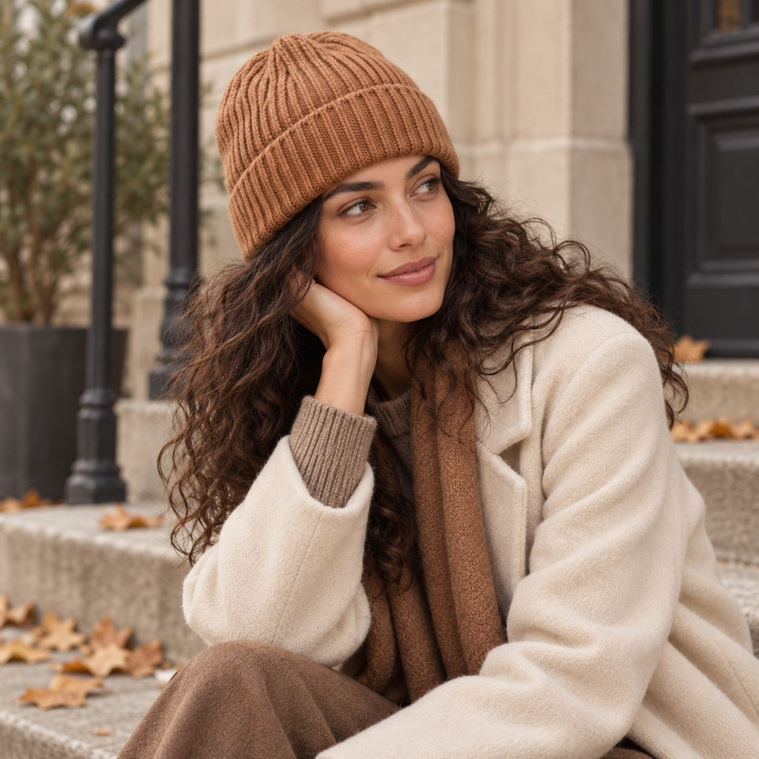Model mit dunkleren Haaren trägt die Cashimar Cashmere Mütze Bari in Vicuna (Rehbraun), kombiniert mit natürlichen Beige- und Brauntönen im herbstlichen Outdoor-Setting.