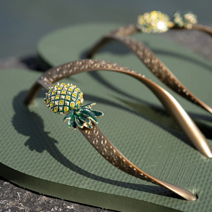 Chanclas by Simone Herrera Livia in Grün, Detailaufnahme der goldenen Straps und des Ananas-Designs der Flip Flops.