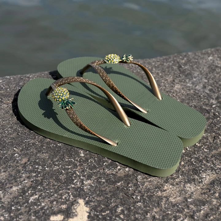 Chanclas by Simone Herrera Livia in Grün mit Ananas-Dekor, Outdoor-Aufnahme der Flip Flops am Wasser.