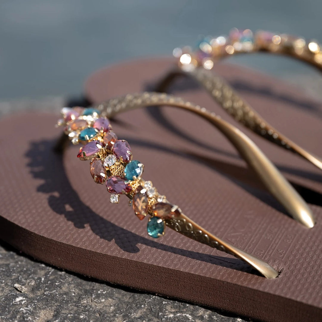 Chanclas by Simone Herrera Chloe in Braun mit türkisen Strasssteinen, Outdoor-Aufnahme der Flip Flops am Wasser.