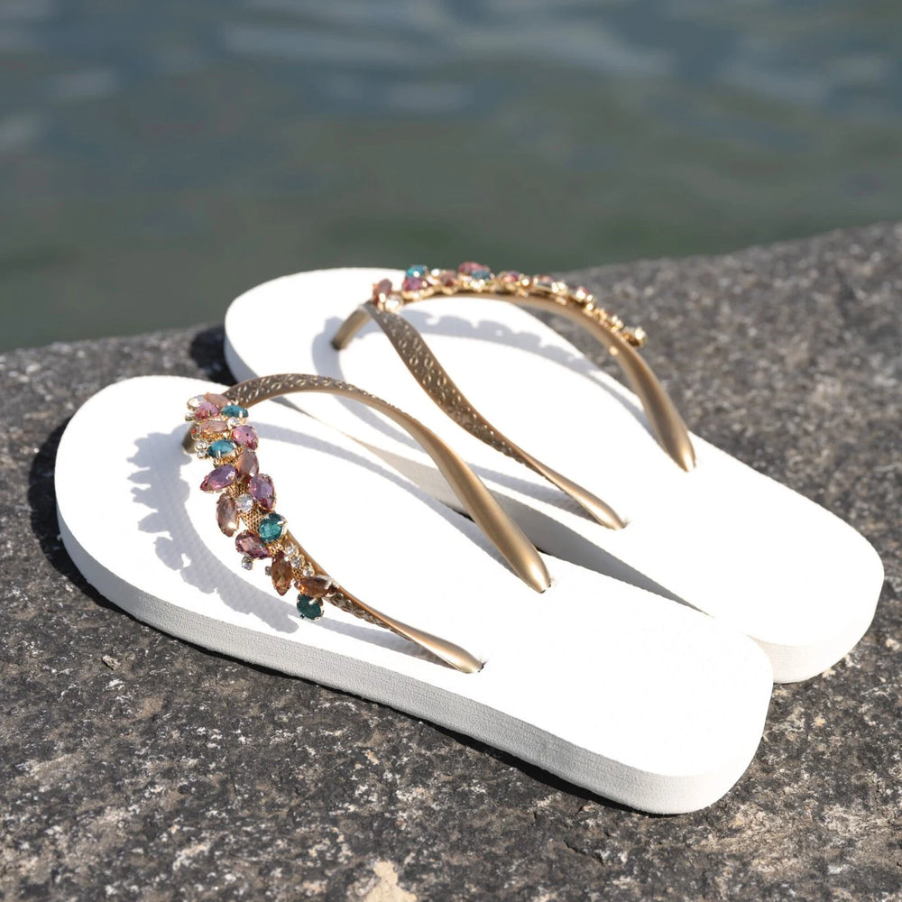 Chanclas by Simone Herrera Chloe in Weiss mit türkisfarbenen Strasssteinen, elegante Damen-Flip-Flops in Outdoor-Aufnahme am Wasser.