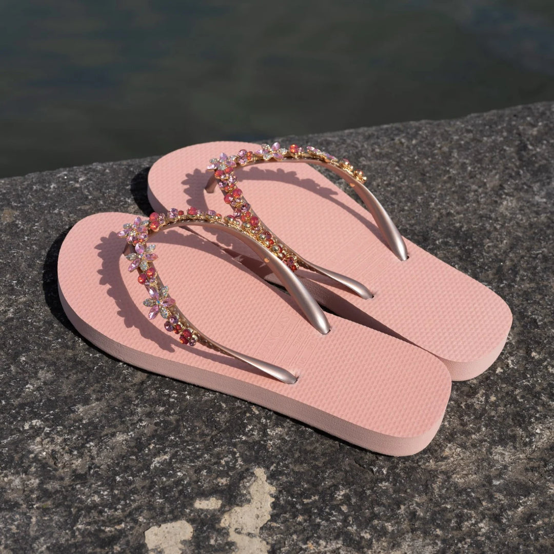 Chanclas by Simone Herrera Valerie in Rose mit Full-Diamond-Straps, elegante Flip Flops leicht schräg auf Stein am Wasser aufgenommen.