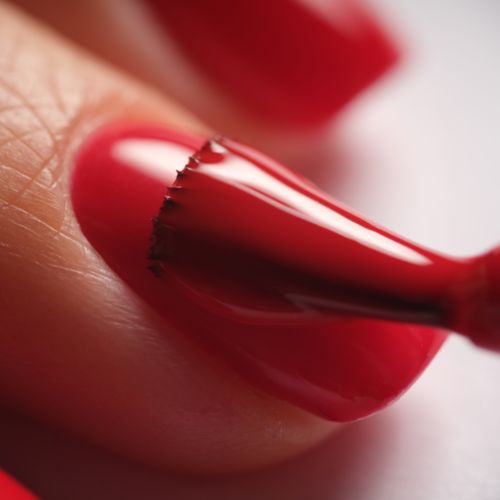 Nahaufnahme: Roter Nagellack wird präzise auf Fingernagel aufgetragen.