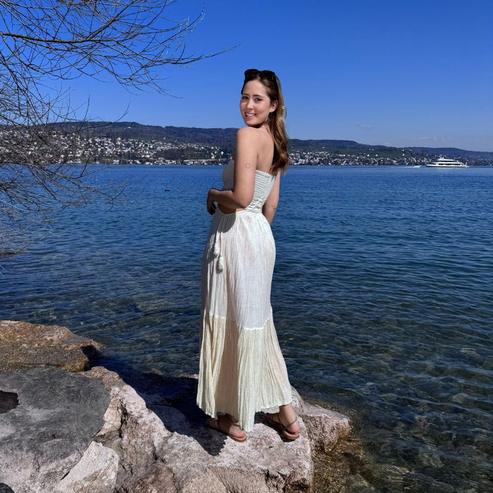D’ARTEMIDE Ava Dress in ivory aus 100 % Baumwolle, langes Sommerkleid mit Cut-Outs, hinten seitlich getragen am Zürichsee auf Felsen
