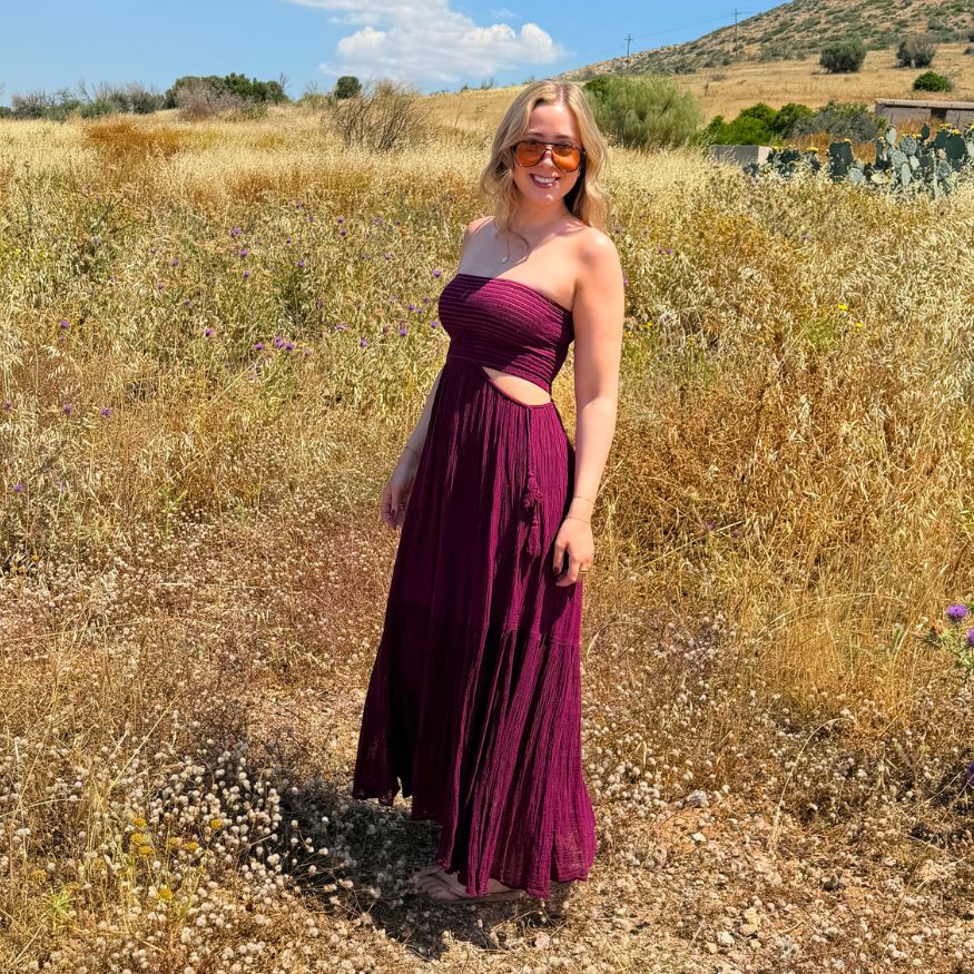 Seitliche Ansicht des D'Artemide Ava Dresses in Wineberry vor sommerlicher Naturkulisse in Griechenland