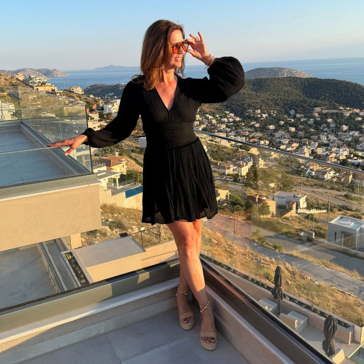 Janine im schwarzen D'Artemide Nephele Mini Dress mit Sandalen auf Terrasse mit mediterraner Aussicht