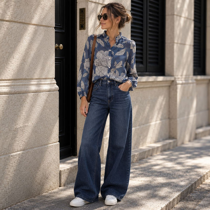 Emotions Bluse Blue Flower aus leichter Baumwolle mit floralem Muster, kombiniert mit dunkelblauen Wide-Leg Jeans, weissen Lemargo Sneakern und brauner Handtasche.