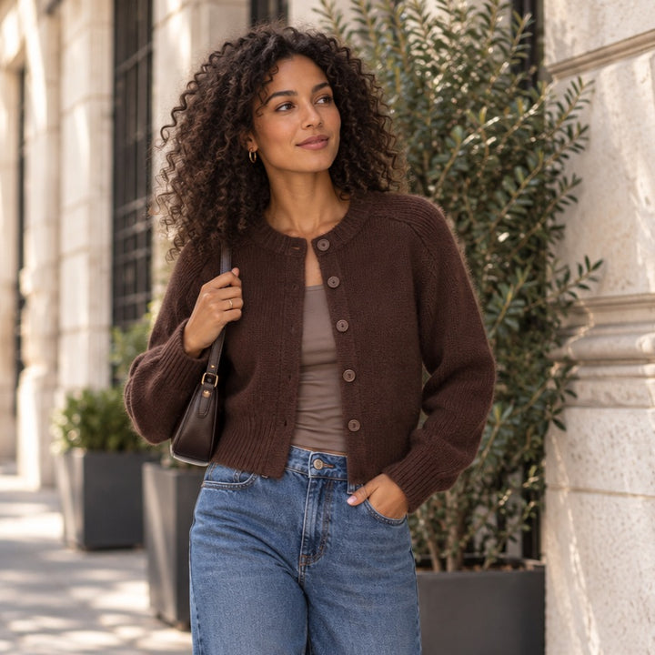 Emotions Cardigan in Choco aus Merinowolle und Cashmere – brauner Damen Cardigan mit Rundhals und Knopfleiste an Model mit dunklen Locken, die eine Jeans trägt und taupefarbenes Top unter dem Pulli