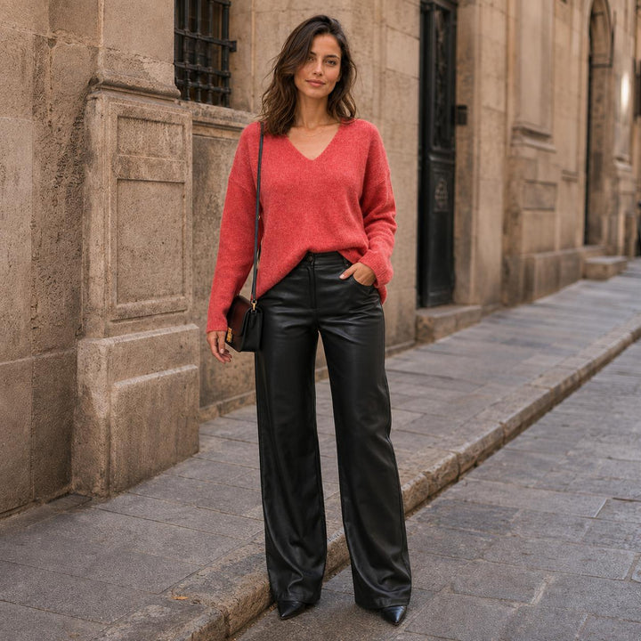 Dunkelhaarige Frau im Emotions V-Pullover in Chili-Rot aus Merinowolle und Cashmere mit schwarzer veganer Lederhose von THE.NIM und schwarzen Highheels und schwarzer Handtasche.