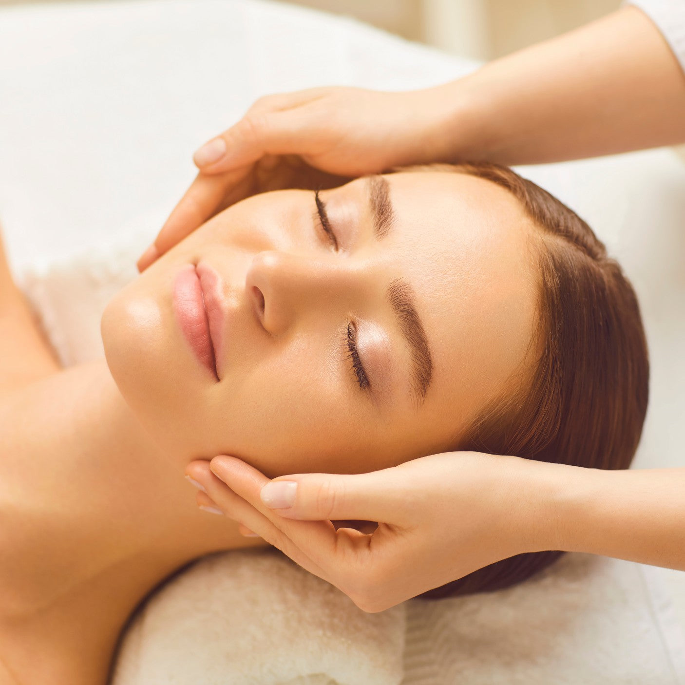 Kosmetikerin führt eine entspannende Gesichtsbehandlung bei einer liegenden Kundin durch.