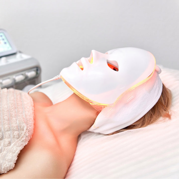 Frau liegt mit einer LED-Gesichtsmaske während einer Hautbehandlung auf der Behandlungsliege.