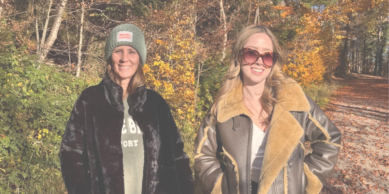 Zwei Frauen in warmen Herbst-Outfits stehen im sonnigen Wald; links eine Frau mit schwarzem Fellmantel und Mütze, rechts eine Frau mit Sonnenbrille und shearlinggefütterter Jacke.