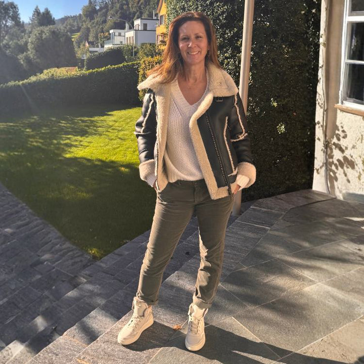 Frau trägt stylische schwarze vegane Lederjacke mit heller Fellinnenseite – Modeinspiration für die Damenmode-Kollektion in Ganzkörperaufnahme.