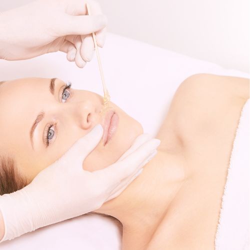 Wachs wird mit einem Spatel auf die Haut im Gesicht einer liegenden Person aufgetragen.