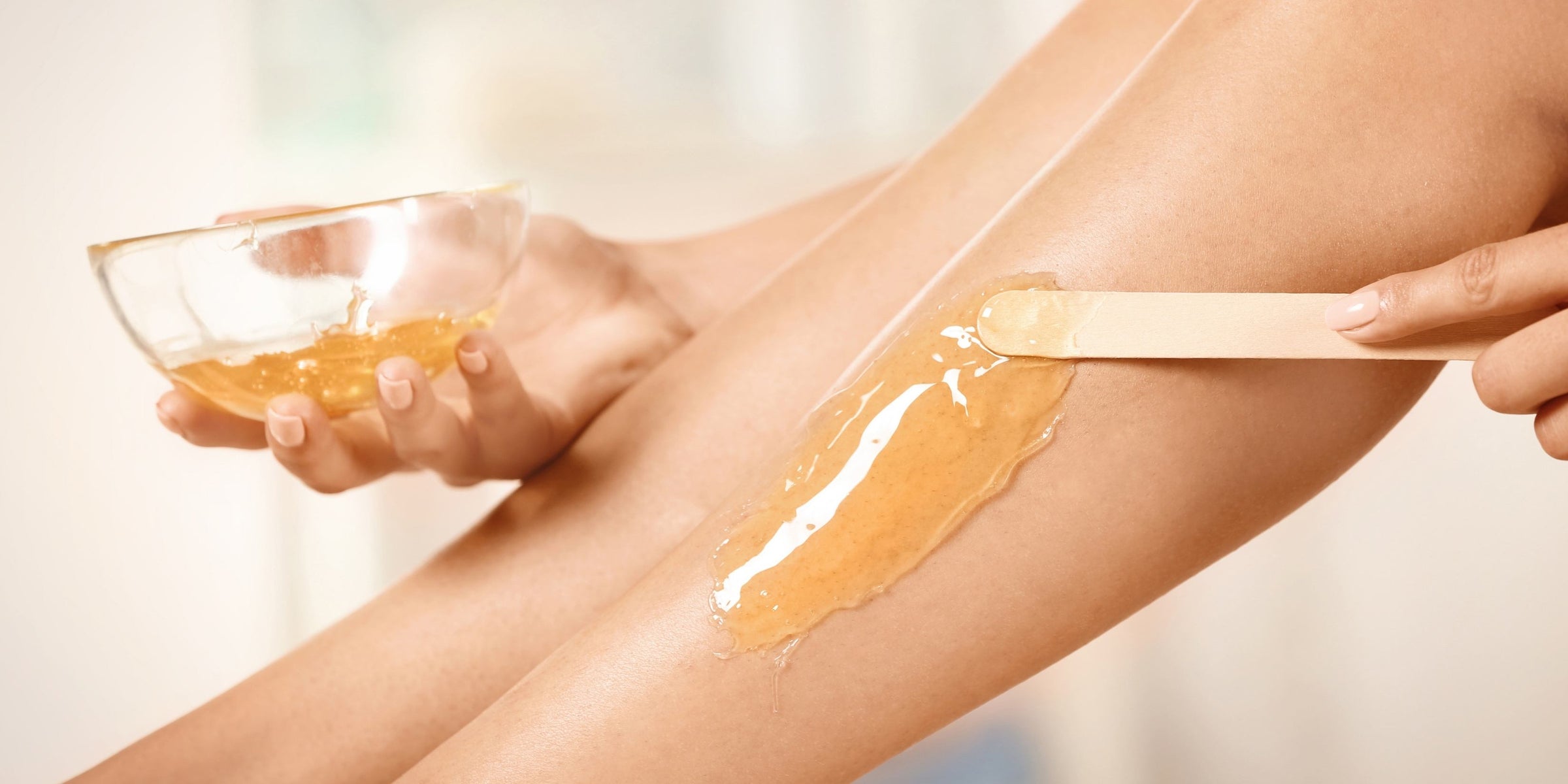 Hand trägt warmes Wachs mit einem Holzspatel auf die Haut eines Beins auf.